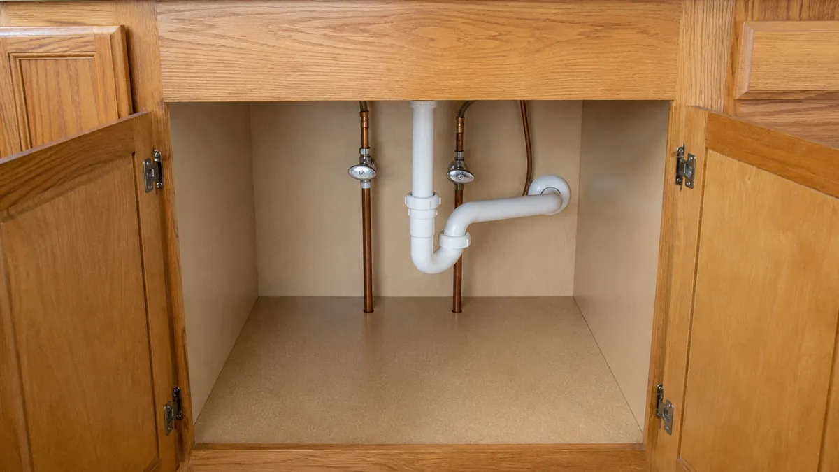 Open cabinet beneath a kitchen sink showing copper supply lines and shutoff valves